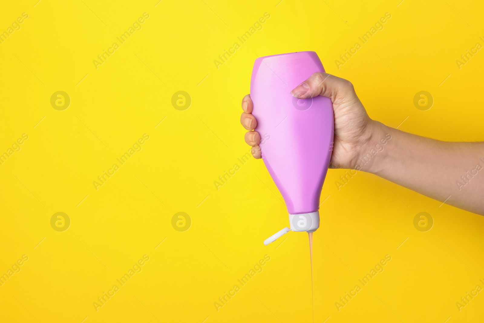 Photo of Woman pouring cosmetic product from bottle on yellow background, closeup. Space for text