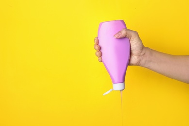 Photo of Woman pouring cosmetic product from bottle on yellow background, closeup. Space for text