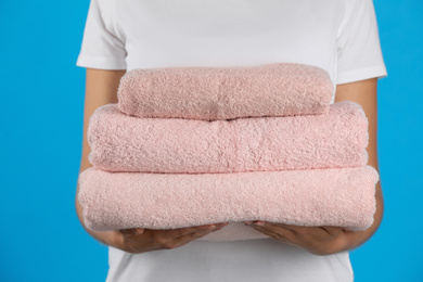 Photo of Woman holding fresh towels on light blue background, closeup