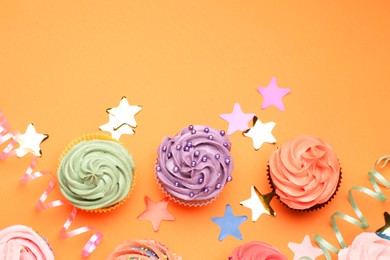 Photo of Delicious cupcakes with bright cream and party decor on orange background, flat lay. Space for text