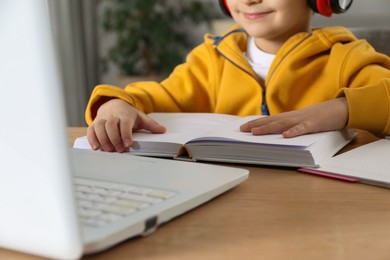 Photo of Cute little boy with modern laptop studying online at home, closeup. E-learning