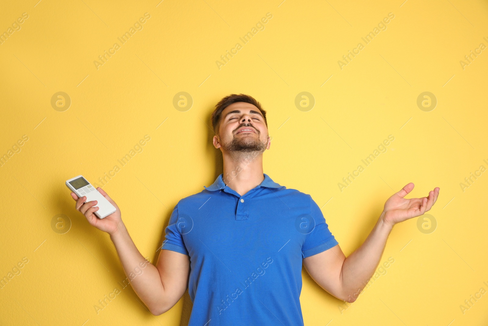 Photo of Happy young man with air conditioner remote control on yellow background