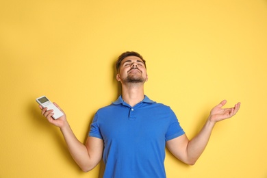 Photo of Happy young man with air conditioner remote control on yellow background