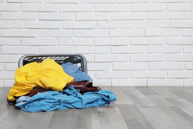 Photo of Laundry basket and dirty clothes on floor near brick wall. Space for text