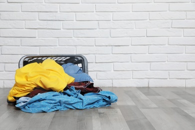 Laundry basket and dirty clothes on floor near brick wall. Space for text