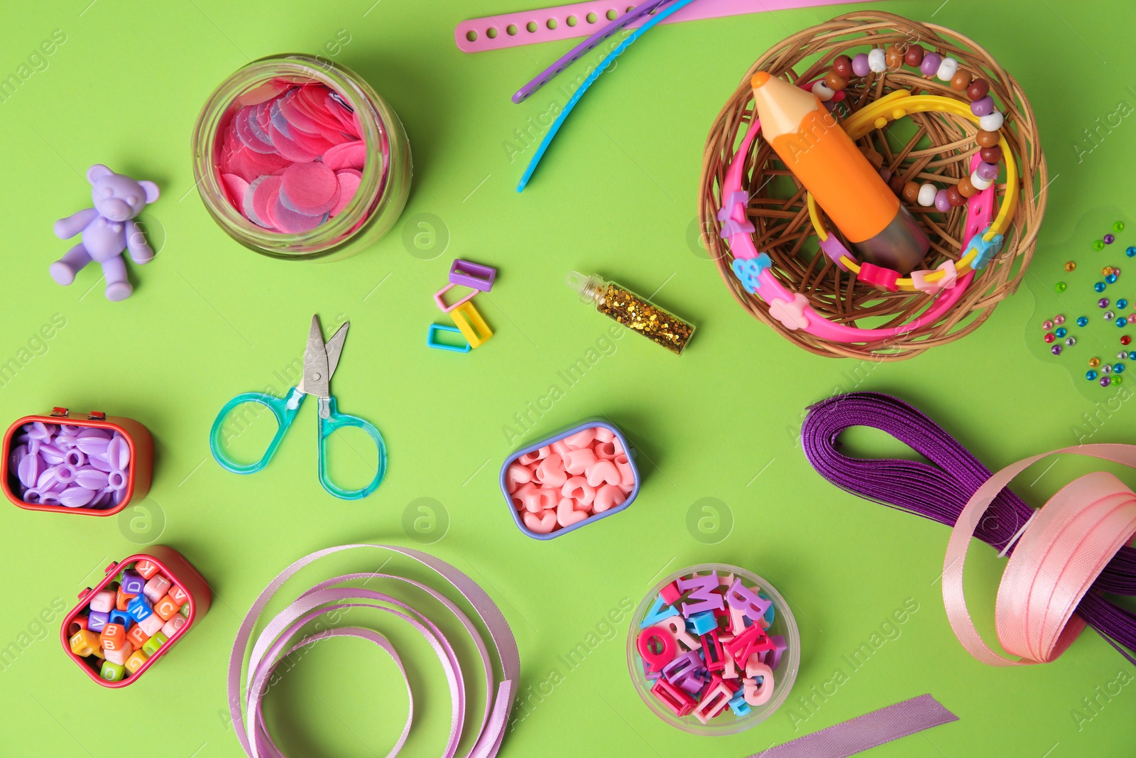 Photo of Handmade jewelry kit for children. Colorful beads, ribbons and supplies on green background, flat lay