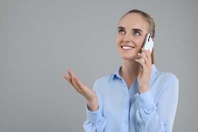 Photo of Happy young secretary talking on smartphone against grey background, space for text