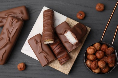 Photo of Pieces of different tasty chocolate bars and hazelnuts on grey wooden table, flat lay