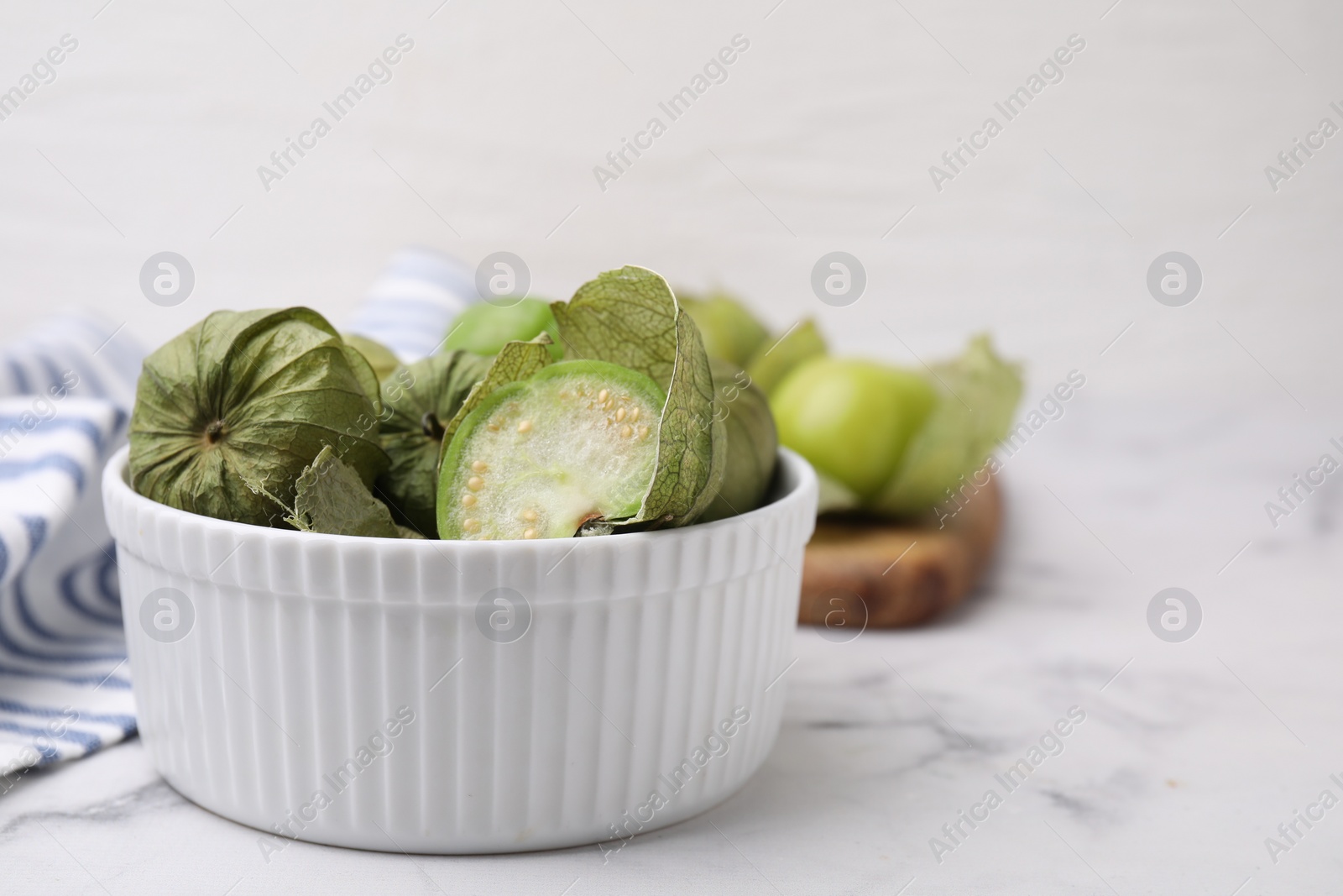 Photo of Fresh green tomatillos with husk in bowl on light marble table, closeup