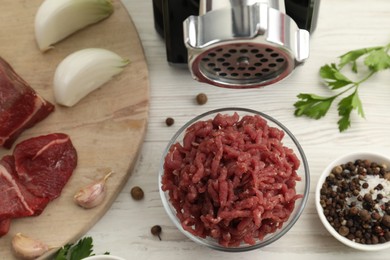 Photo of Meat grinder, beef, onion, garlic, parsley and spices on white wooden table, flat lay