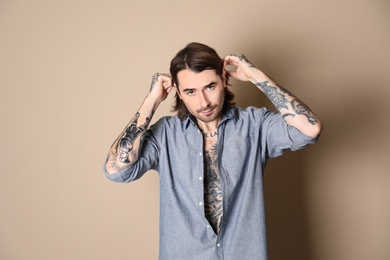 Young man with tattoos on body against beige background