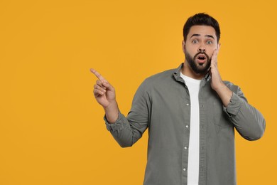 Special promotion. Surprised man pointing at something on orange background. Space for text