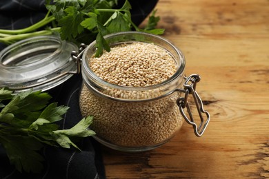 Photo of Dry quinoa seeds in glass jar and parsley on wooden table, closeup