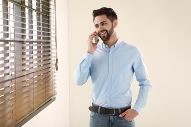 Photo of Handsome man talking on mobile phone at window indoors