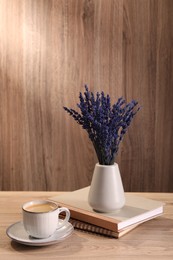 Bouquet of beautiful preserved lavender flowers, notebooks and cup of coffee on wooden table indoors