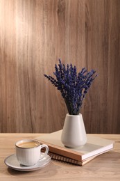 Photo of Bouquet of beautiful preserved lavender flowers, notebooks and cup of coffee on wooden table indoors