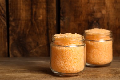 Photo of Jars with orange sea salt on wooden table. Space for text