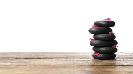 Photo of Stack of spa stones and flower petals on wooden table against white background. Space for text