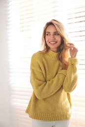 Photo of Beautiful young woman wearing warm yellow sweater near window at home
