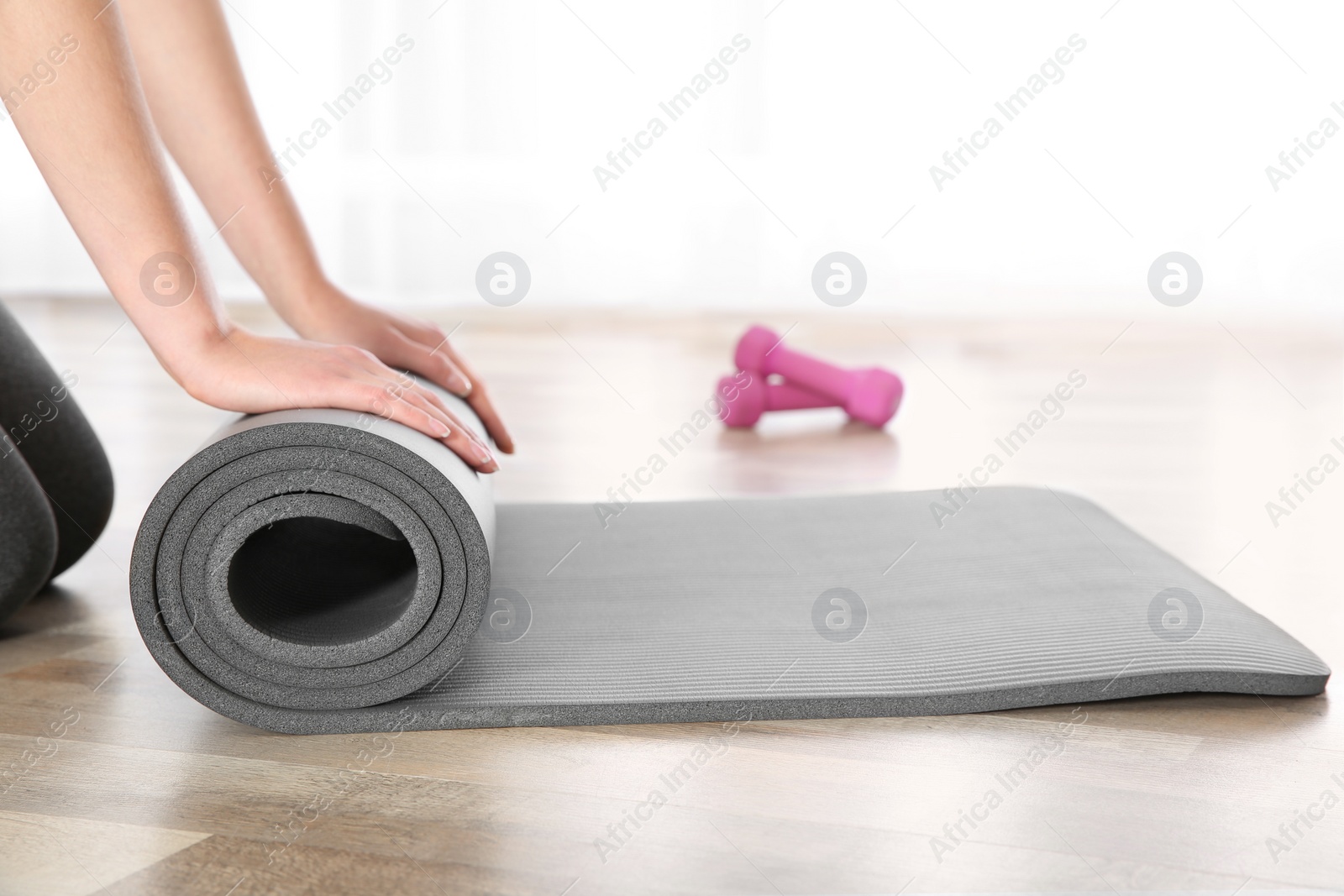 Photo of Woman rolling yoga mat on floor indoors, closeup