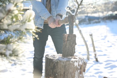 Photo of Man chopping wood with axe outdoors on winter day, closeup