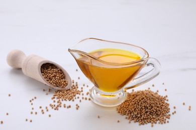 Photo of Jug of natural oil and mustard seeds on white table