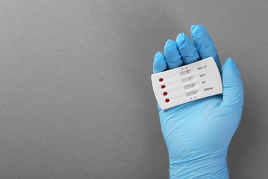 Doctor holding disposable multi-infection express test on light grey background, top view. Space for text