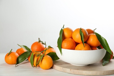 Fresh ripe tangerines with green leaves on white wooden table