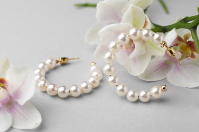 Elegant pearl earrings and orchid flowers on white background, closeup