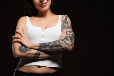 Beautiful woman with tattoos on arms against black background, closeup. Space for text