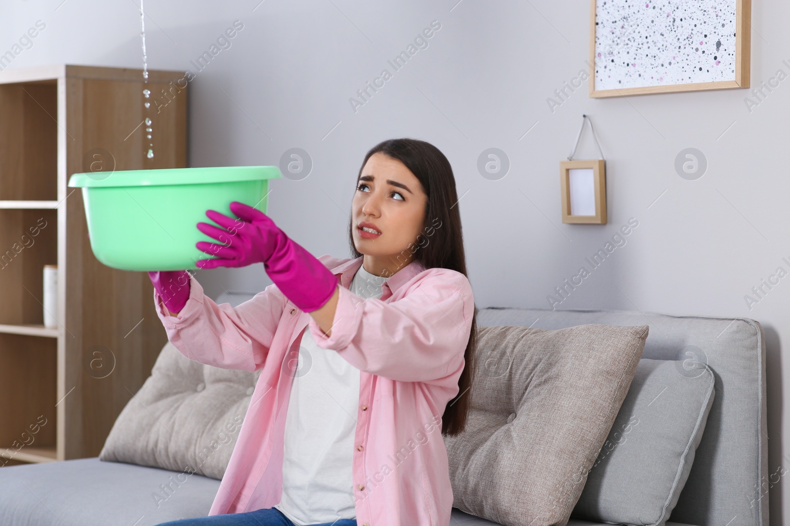 Photo of Young woman collecting leaking water from ceiling at home. Time to call roof repair service