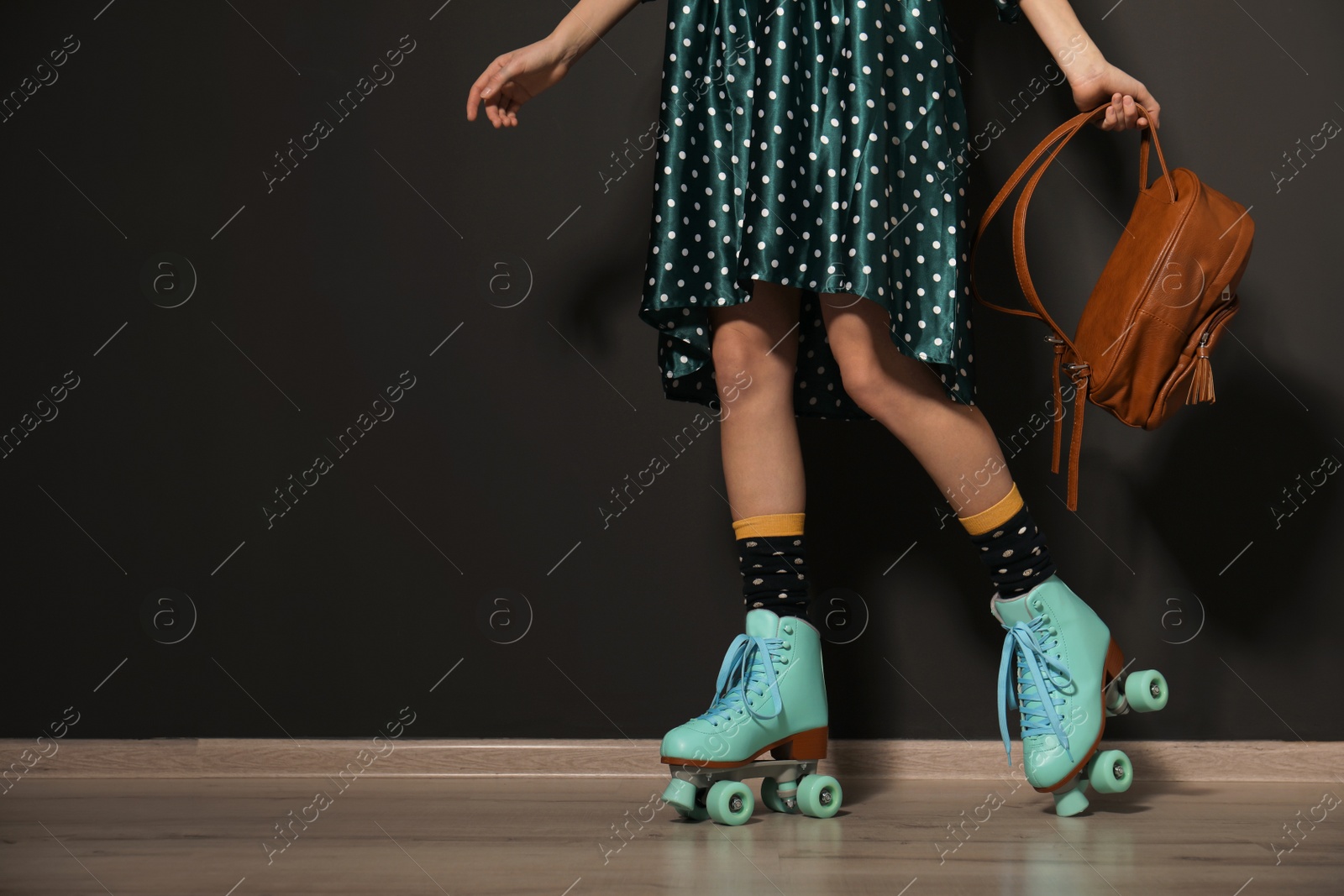 Photo of Young woman with retro roller skates against black wall, closeup. Space for text