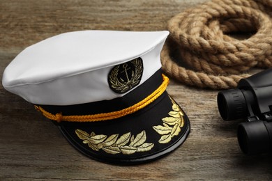 Peaked cap, rope and binoculars on wooden background
