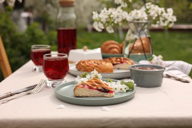 Stylish table setting with beautiful spring flowers, fruit drink and pie in garden