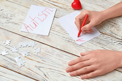 Woman writing word AUTISM on paper on wooden background