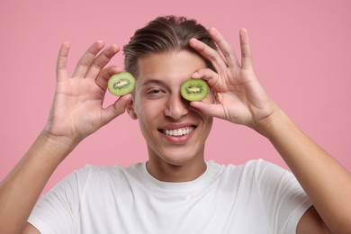 Photo of Smiling man covering eye with halfkiwi on pink background