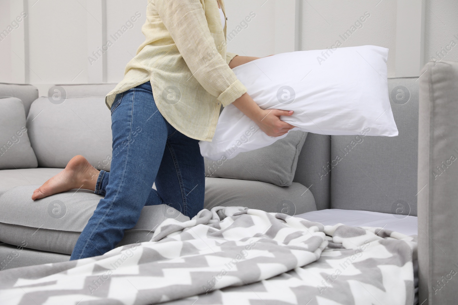 Photo of Woman making sleeping place for guest in living room, closeup. Convertible sofa