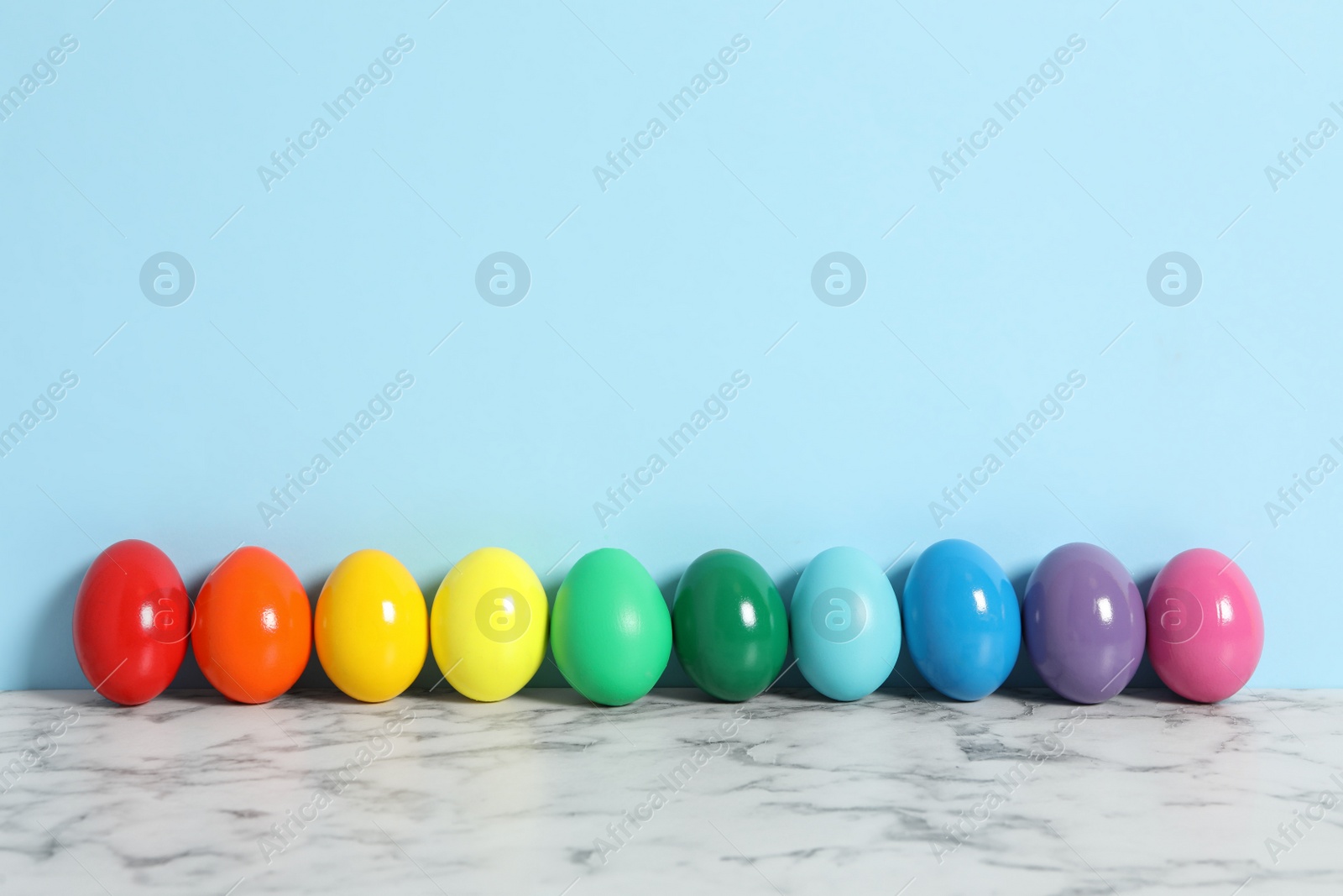 Photo of Easter eggs on white marble table against light blue background, space for text