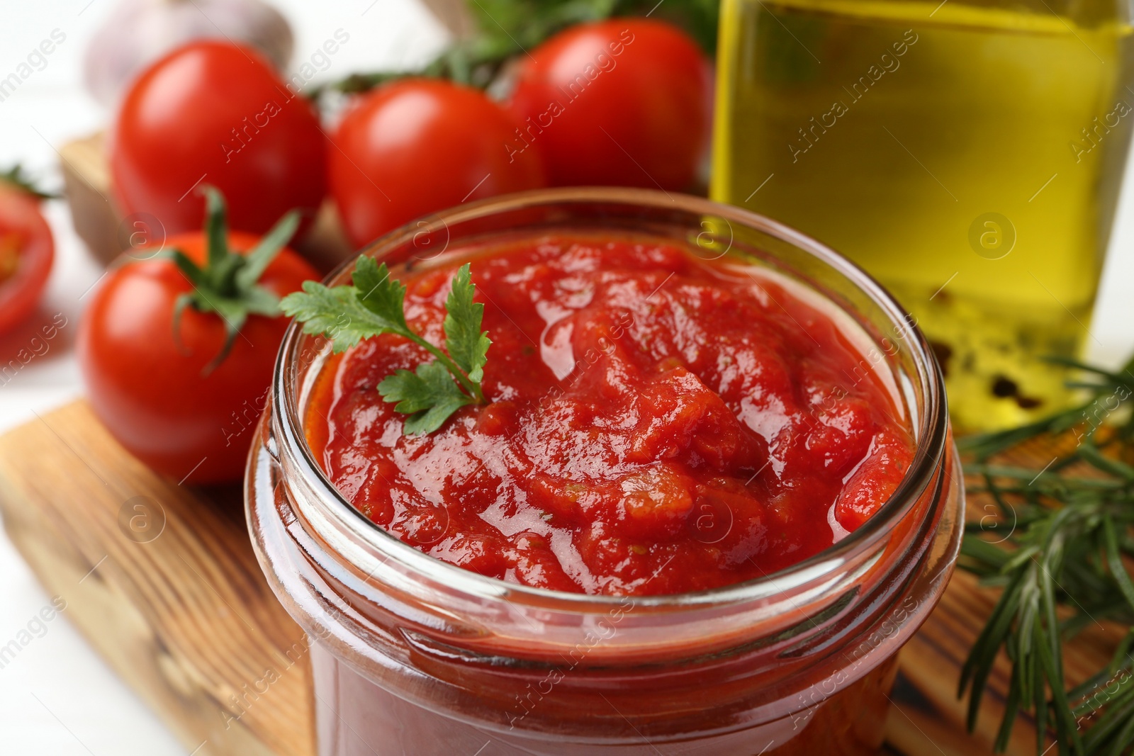 Photo of Homemade tomato sauce and parsley in jar on white table, closeup