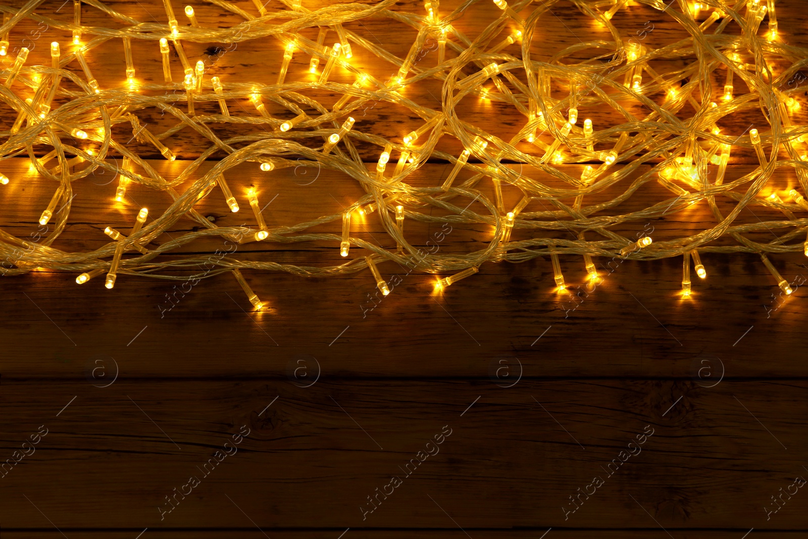 Photo of Glowing Christmas lights on wooden background, top view. Space for text