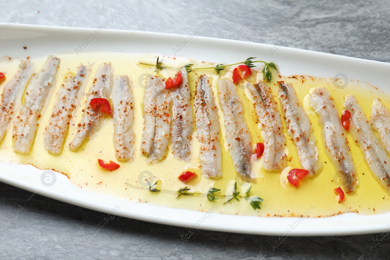 Photo of Tasty pickled anchovies with spices on gray table, closeup