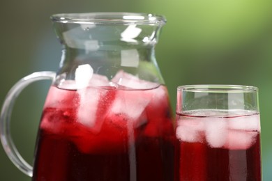 Refreshing hibiscus tea with ice cubes on blurred green background, closeup