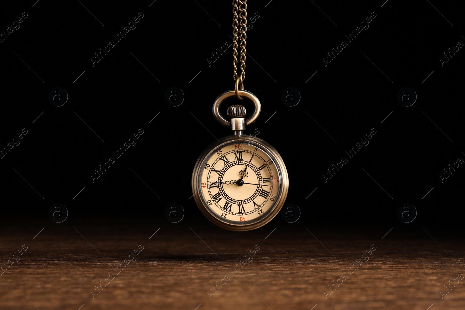 Photo of Stylish pendulum above wooden table on black background. Hypnotherapy session