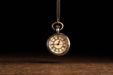 Stylish pendulum above wooden table on black background. Hypnotherapy session