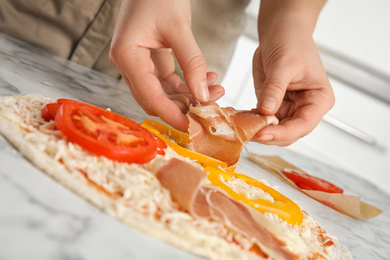 Photo of Woman adding prosciutto to pizza white marble table, closeup