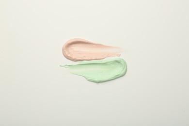 Strokes of pink and green color correcting concealers on white background, top view