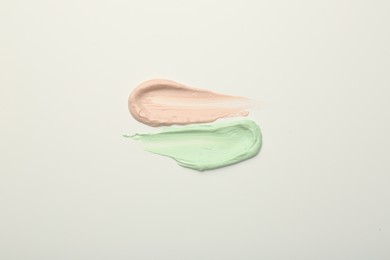 Photo of Strokes of pink and green color correcting concealers on white background, top view