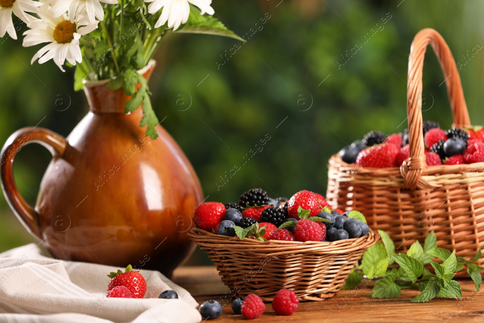 Photo of Different fresh ripe berries and beautiful flowers on wooden table outdoors