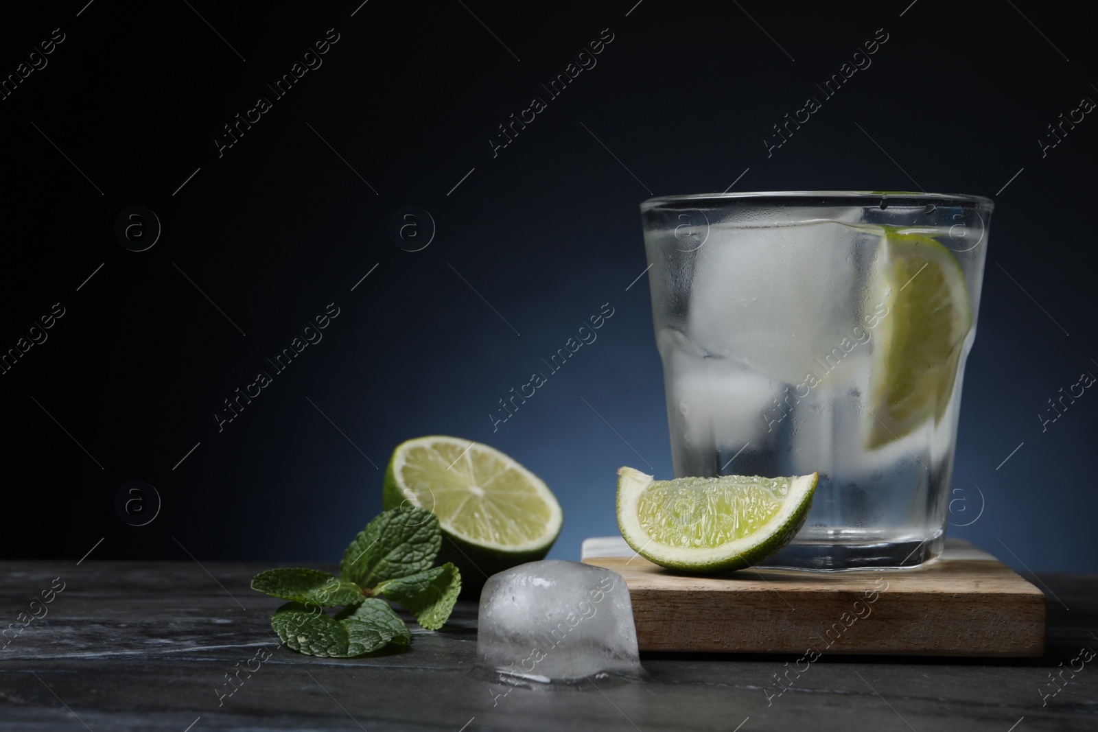 Photo of Glass of vodka with lime and ice on black marble table. Space for text