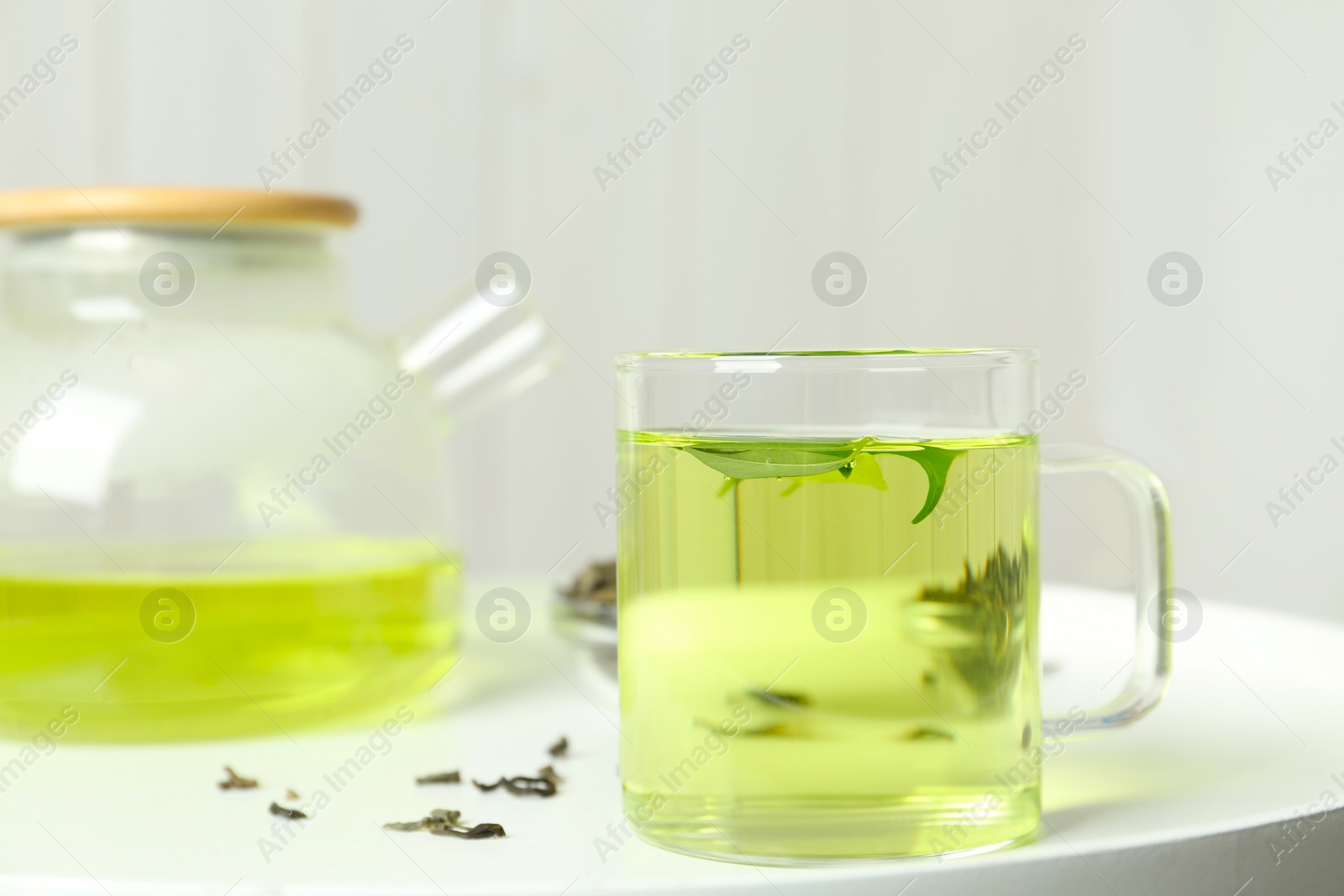 Photo of Cup of aromatic green tea with leaves on white table